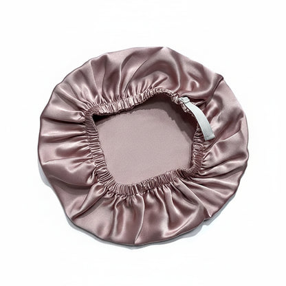A satin sleep cap in a dusty rose pink color, laid flat on a white background. It features an elasticized opening with a white drawstring.